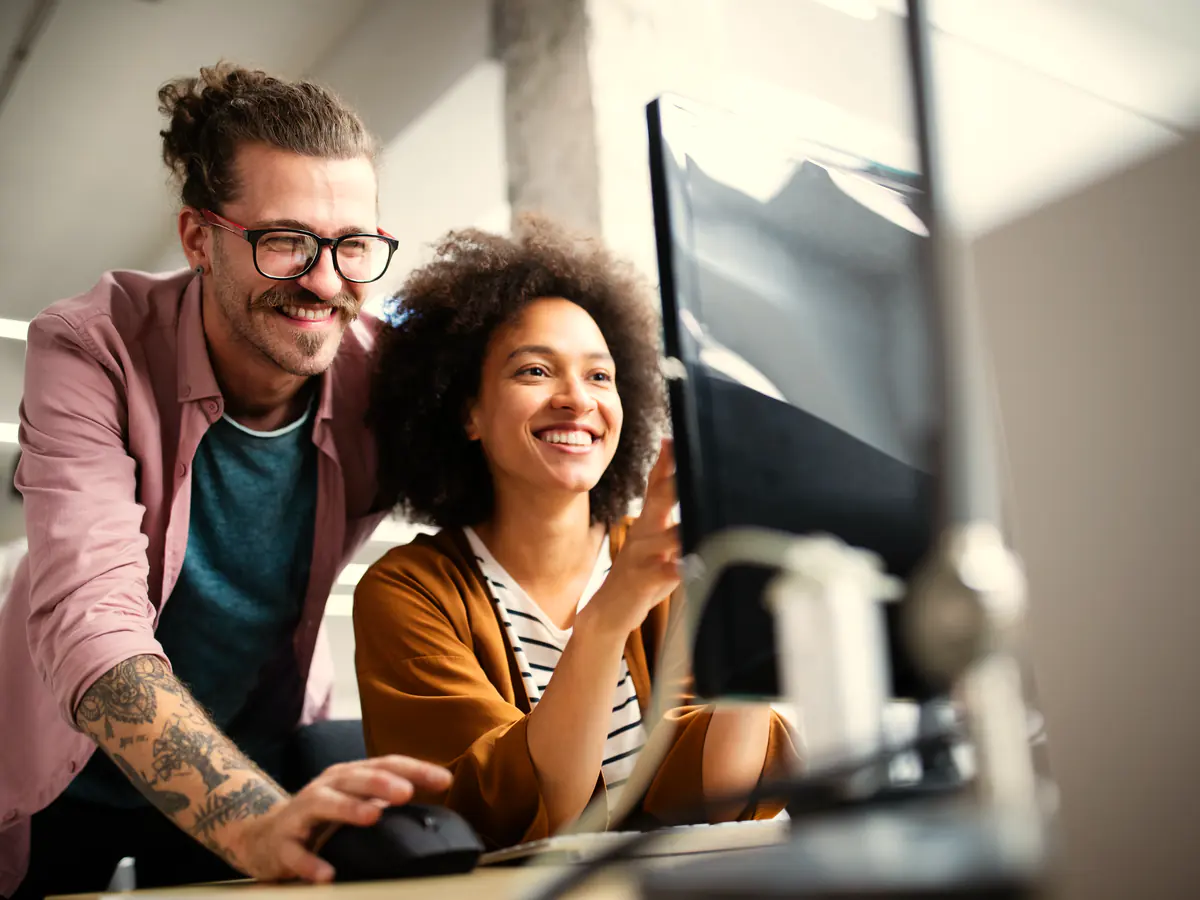 Two colleagues smiling as they review customer records on screen