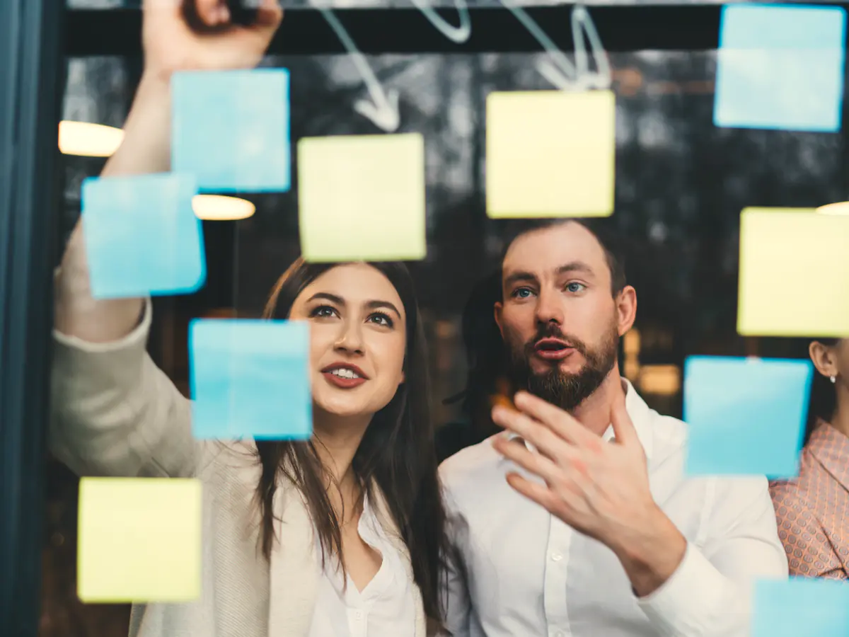 Marketers planning a workflow with sticky notes on a glass wall