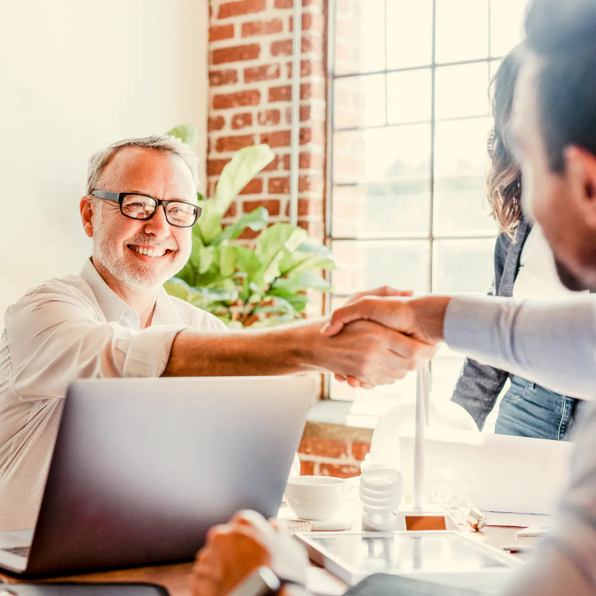 A smiling salesperson shaking hands with a client across a desk