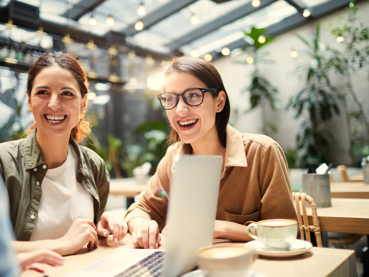 Two colleagues smiling as they review a website on a laptop